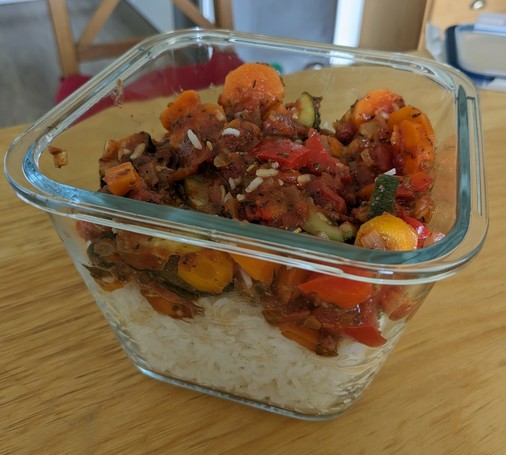 Reste einer Gemüsepfanne mit Zucchini, Paprika, Möhren und Tomaten auf Reis in einer Glasschüssel.