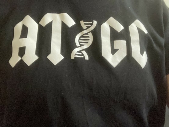 Aufdruck auf einem schwarzen T-Shirt: ATGC im ACDC-Stil, zwischen dem T und dem G befindet sich eine DNA-Doppelhelix