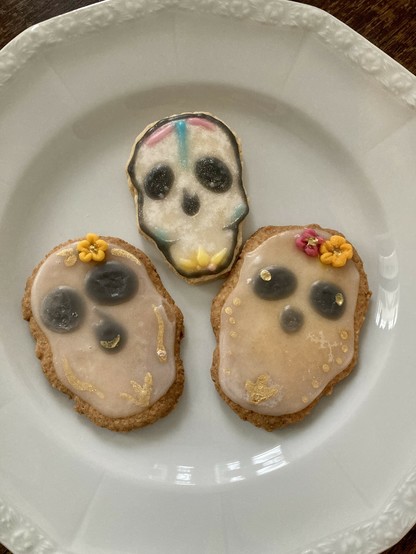 auf einem weißen Teller liegen drei bunt verzierte Kekse in Form von Totenköpfen