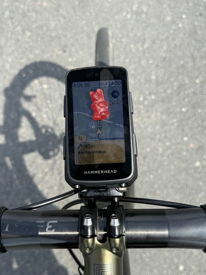 A bike's handlebars with a mounted GPS displaying a navigation screen, partly obscured by a red gummy bear on the screen.