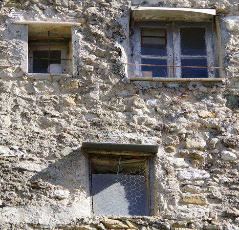 Drei genormte Fenster in einer verputzten Häuserwand.