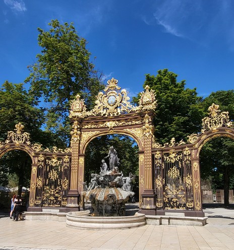 Ein übiger Springbrunnen in einen nich übigrren verzierten gusseisenen Tor mit viel vergoldeten Elementen.