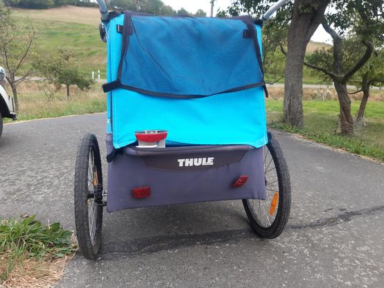 Blauer Thule Fahrradanhäger aus dem links im unteren Drittel zwischen den Stoffen ein Rücklicht mit großem Reflektor herausschaut.