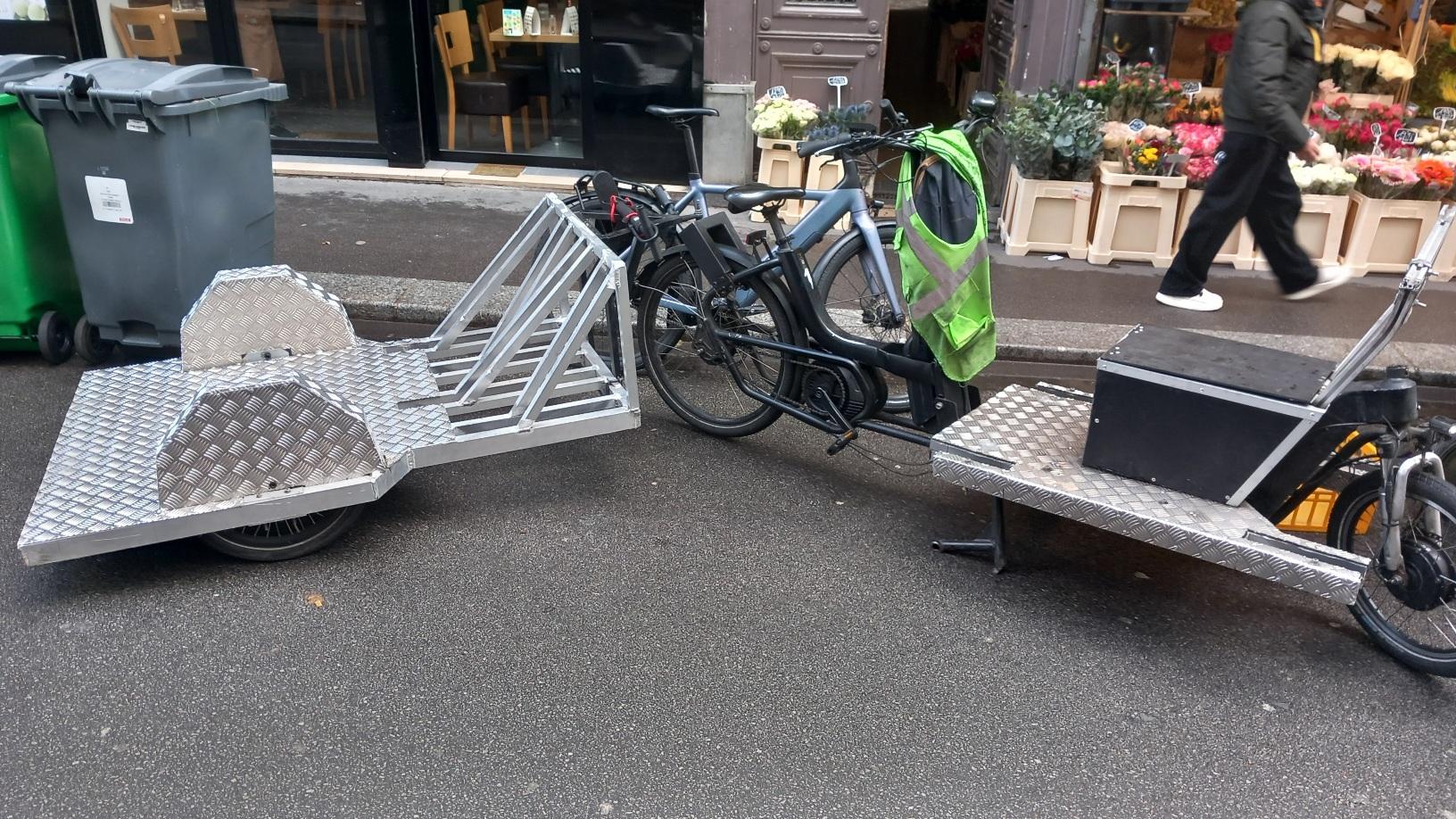 Lastenfahrrad mit Anhänger vor Fahrrad und Blumengeschäft sowie Mülltonnen