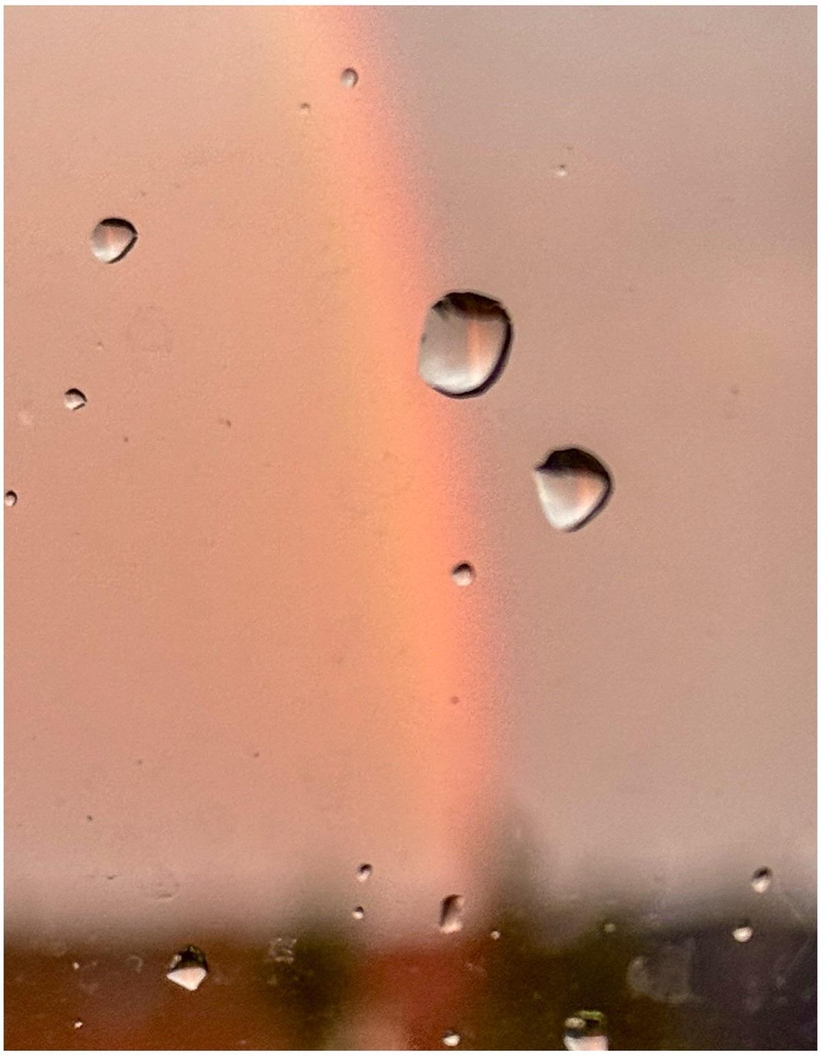 An out-of-focus image featuring raindrops on a window with a faint rainbow appearing in the background. The scene has a soft, muted color palette. An out-of-focus image featuring raindrops on a window with a faint rainbow appearing in the background. The scene has a soft, muted color palette.