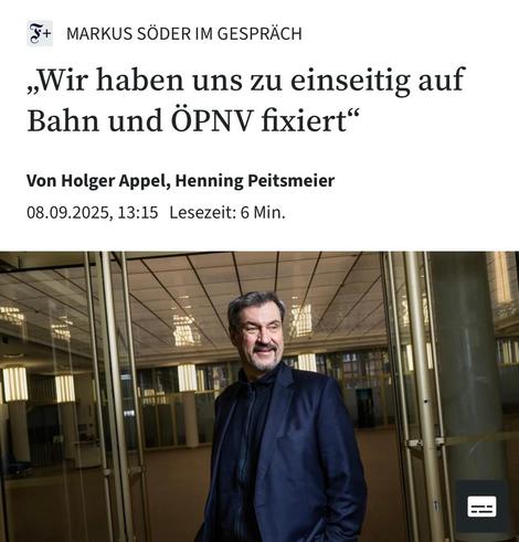 Das Bild zeigt eine Online-Artikelvorlage mit dem Titel „Wir haben uns zu einseitig auf Bahn und ÖPNV fixiert“ Im oberen Bereich des Bildes ist der Name „Markus Söder im Gespräch“ zu sehen. Darunter ist ein Foto eines Mannes in einem dunkelblauen Anzug, der lächelnd in einem modernen, offenen Raum mit Glaswänden und einer hohen, beleuchteten Decke steht.