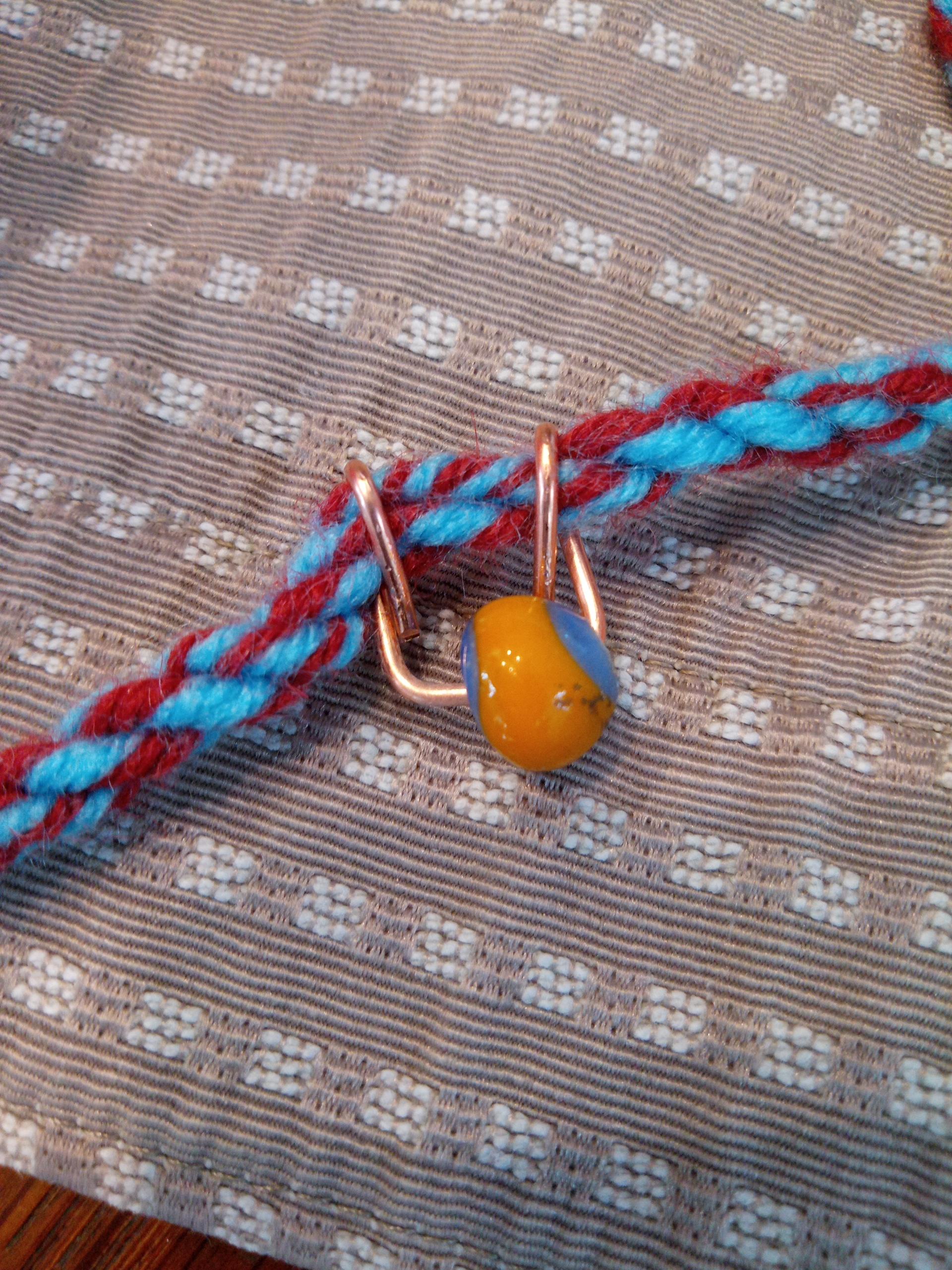 Eine blauorange Glasperle hängt an einem blaurot verzwirntem Seil.