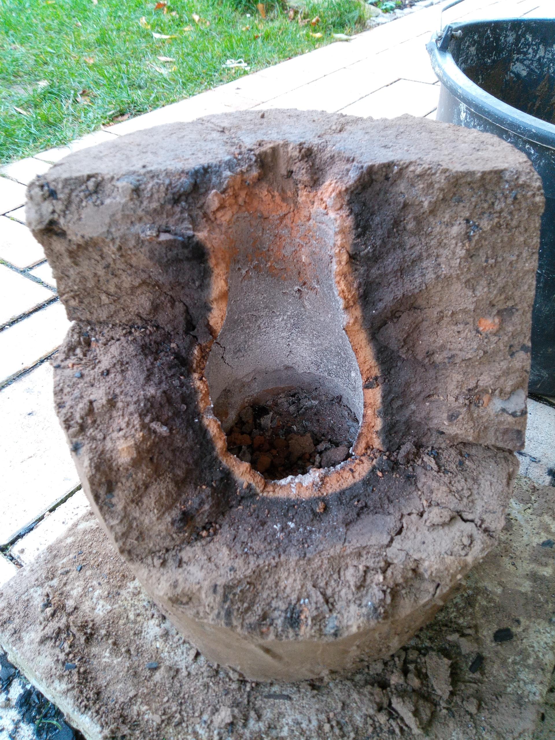 Der Ofen wurde für den Rücktransport wieder zerlegt. Man sieht hier in das Innere des Ofens: Ein ca. 8cm breiter Brennraum, der sich flaschenförmig nach oben verjüngt (Venturi-Effekt). Gut zu erkennen die etwa 1cm dicke rote Verziegelung der kompletten Innenwand, gefolgt von etwa 3cm dunkel gebranntem Lehm, und außen herum die lehmfarbene Hülle.