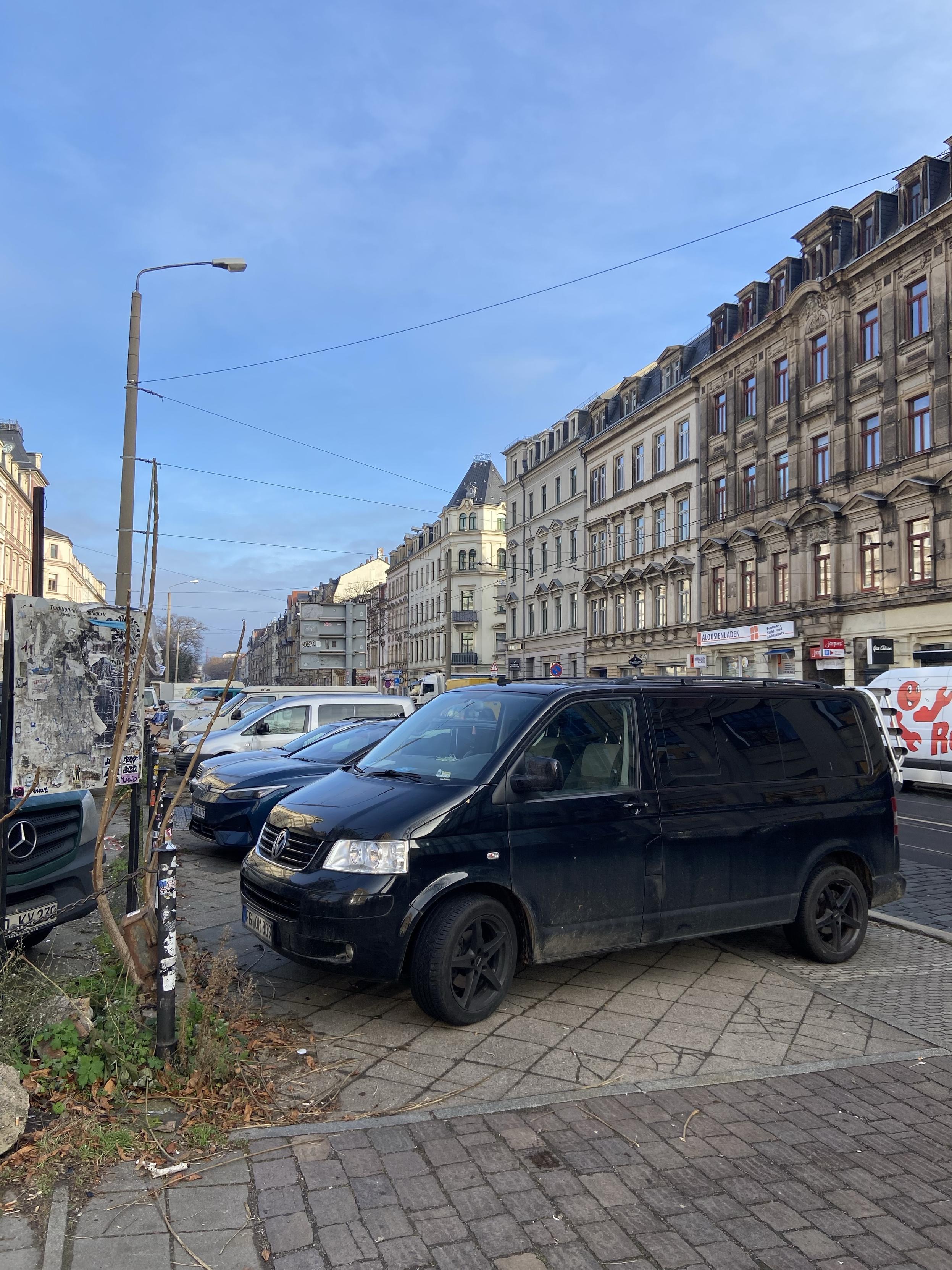 Etliche querparkende Stehzeuge blockieren einen Fußweg in voller Breite an einer Hauptstraße. 