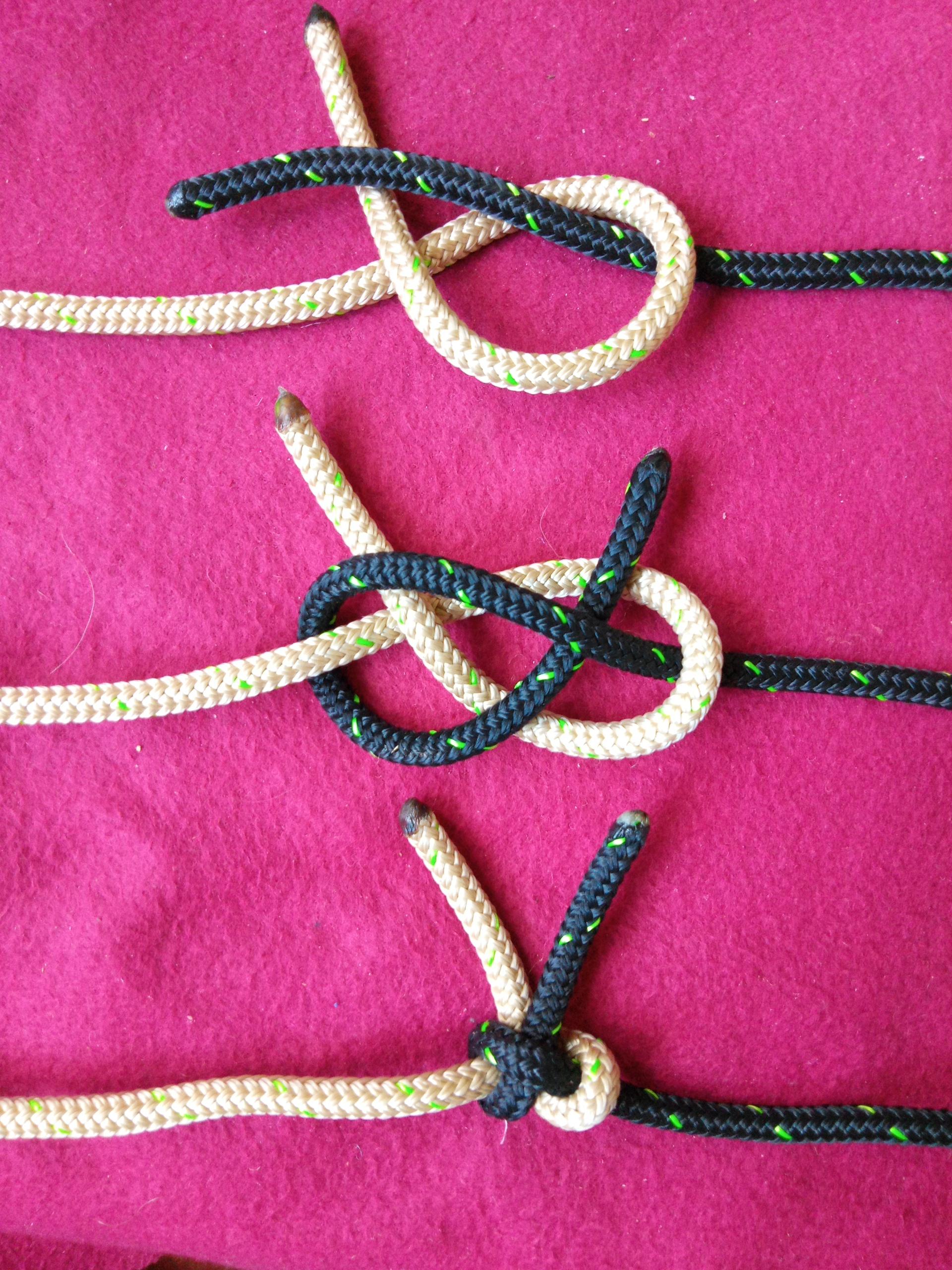 Das Foto zeigt zwei Zwischenschitte und ganz unten den dichtgeholten Knoten. Die beiden Seile sind schwarz und weiß und lassen sich deshalb gut auseinanderhalten. Alles ist auf einer violettroten Decke fotografiert.