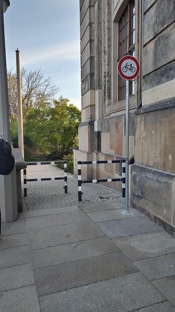 Ein Verbitsschild für Fahrräder neben einem schmalen Durchgang mit Umlaufsperre. 