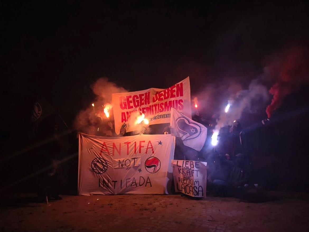 Mobshot im Dunkeln mit Transpis: vorn mitte "Liebe und Kraft für Reclaim LaCasa", links daneben "Anfifa not Intifada", drüber dahinter "Gegen jeden Antisemitismus". die Transpis sind umrahmt von Menschen, einige halten Bengalos