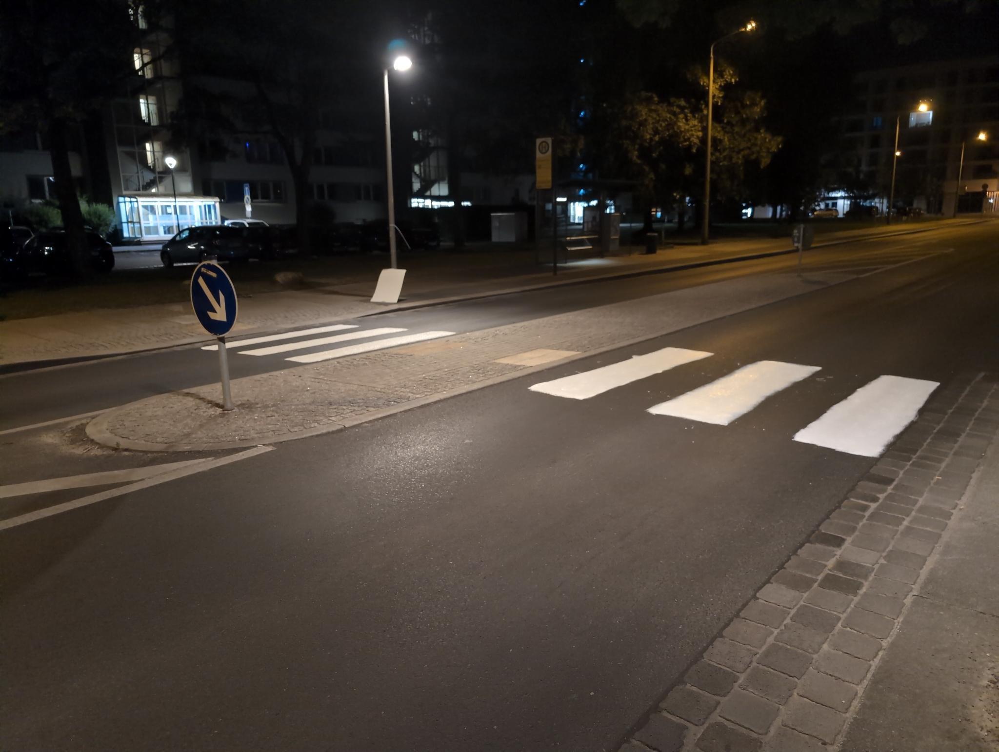 Die Pfotenhauerstraße mit Zebrastreifen bei Nacht. Zwischen abgesenkten Bordsteinen sind je drei weiße Streifen pro Fahrbahn auf die Straße gemalt, dazwischen liegt eine langgezogene Verkehrsinsel. Im Hintergrund ist ein Bushäuschen der Haltestelle Böhnischplatz zu sehen.