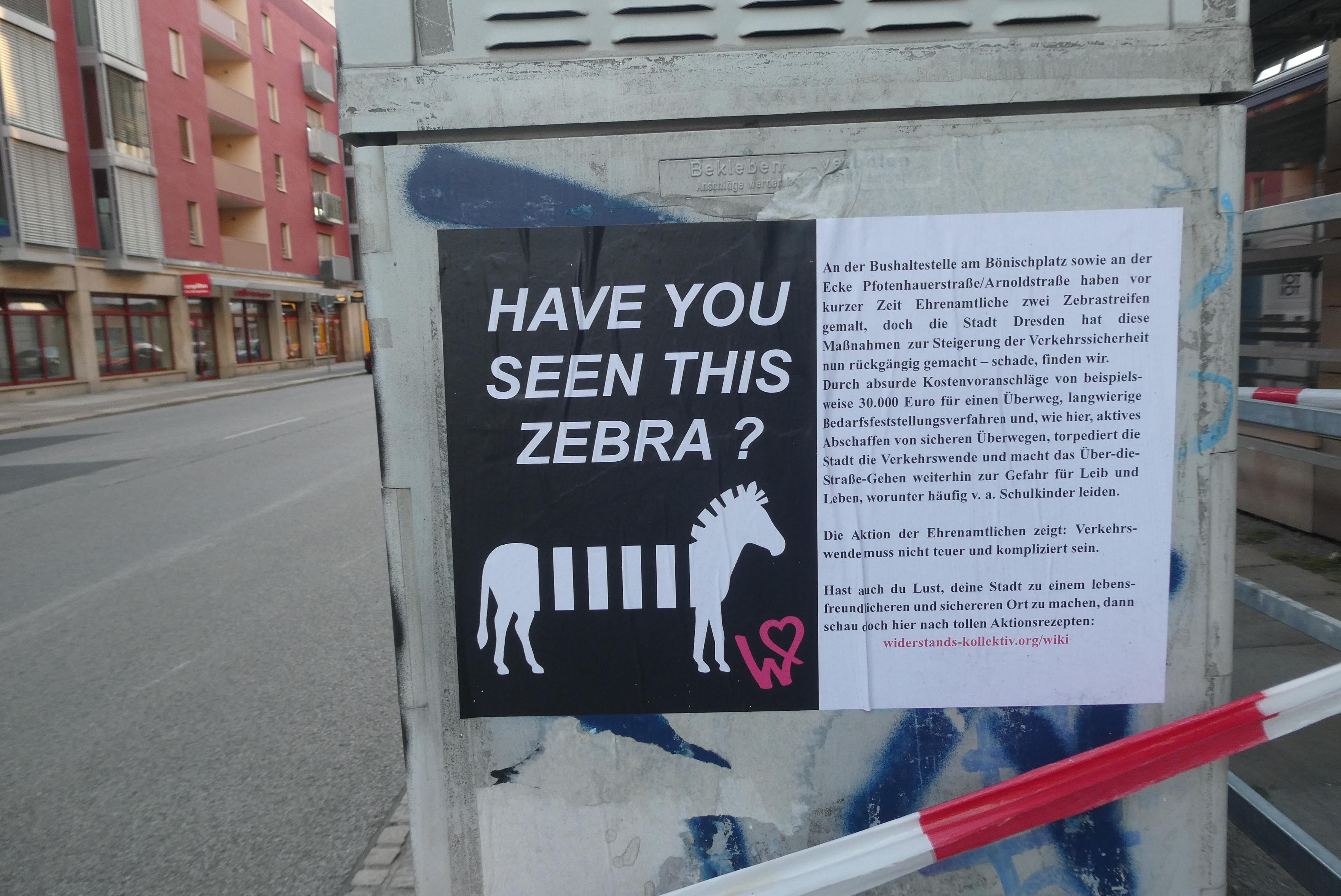 Ein Plakat klebt auf einem grauen Kasten, auf dem oben schwach "Bekleben verboten" steht. Das Plakat ist im Querformat und zweispaltig. Die linke Seite ist schwarz, in weiß steht groß die Frage "HAVE YOU SEEN THIS ZEBRA?", in weiß ein stilisiertes Zebra, uns in pink das Logo des Widerstandskollektivs: ein W, das in einem Herz endet. Auf der rechten Seite steht schwarzer Text auf weißem Grund, der die Aktionen erklärt und ein Link zu Aktionsrezepten: widerstands-kollektiv.org/wiki