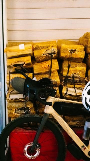 The front of a bike with a wooden frame, which leans against a stack of firewood. 