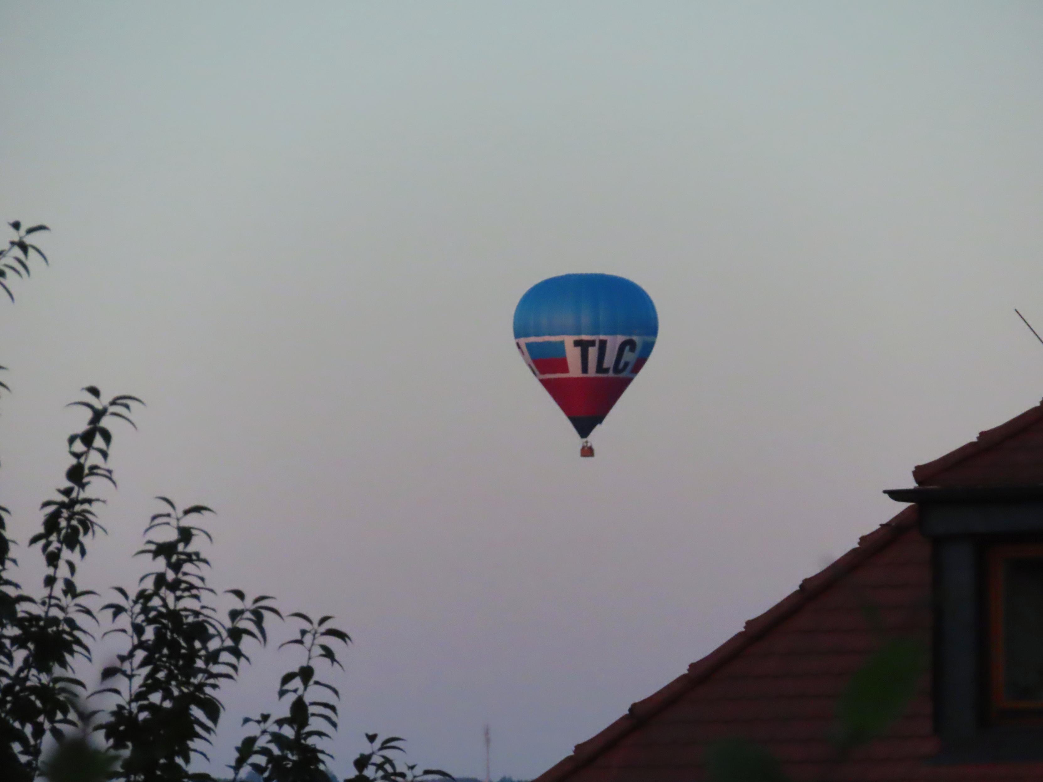 Morgendämmerung.

Zwischen Baum, links, und Hausdach ist ein BlauWeißRoter Heißluftballon zu sehen.