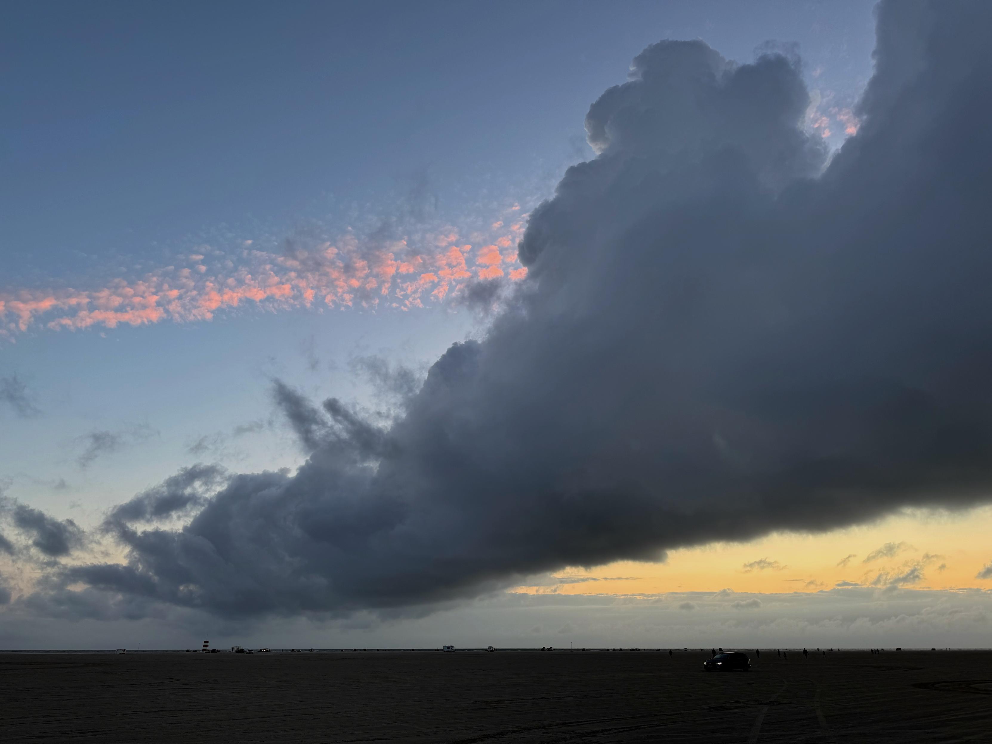 Dunkle Wolke diagonal am Abendhimmel, dahinter gelbe und rötlich scheinen Wolken