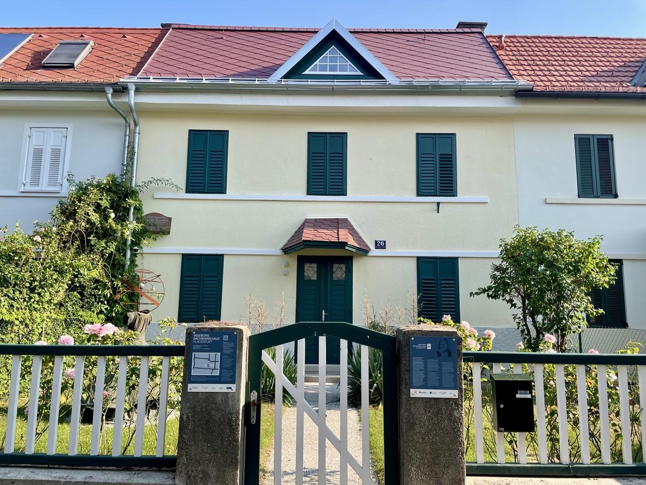 Das Haus Henselstraße 26: ein Reihenhaus, zweistöckig plus Dach, die geschlossenen Fensterläden versuchen der Hitze zu trotzen, Vorgarten, Gartenpforte und rechts und links davon ein Schild