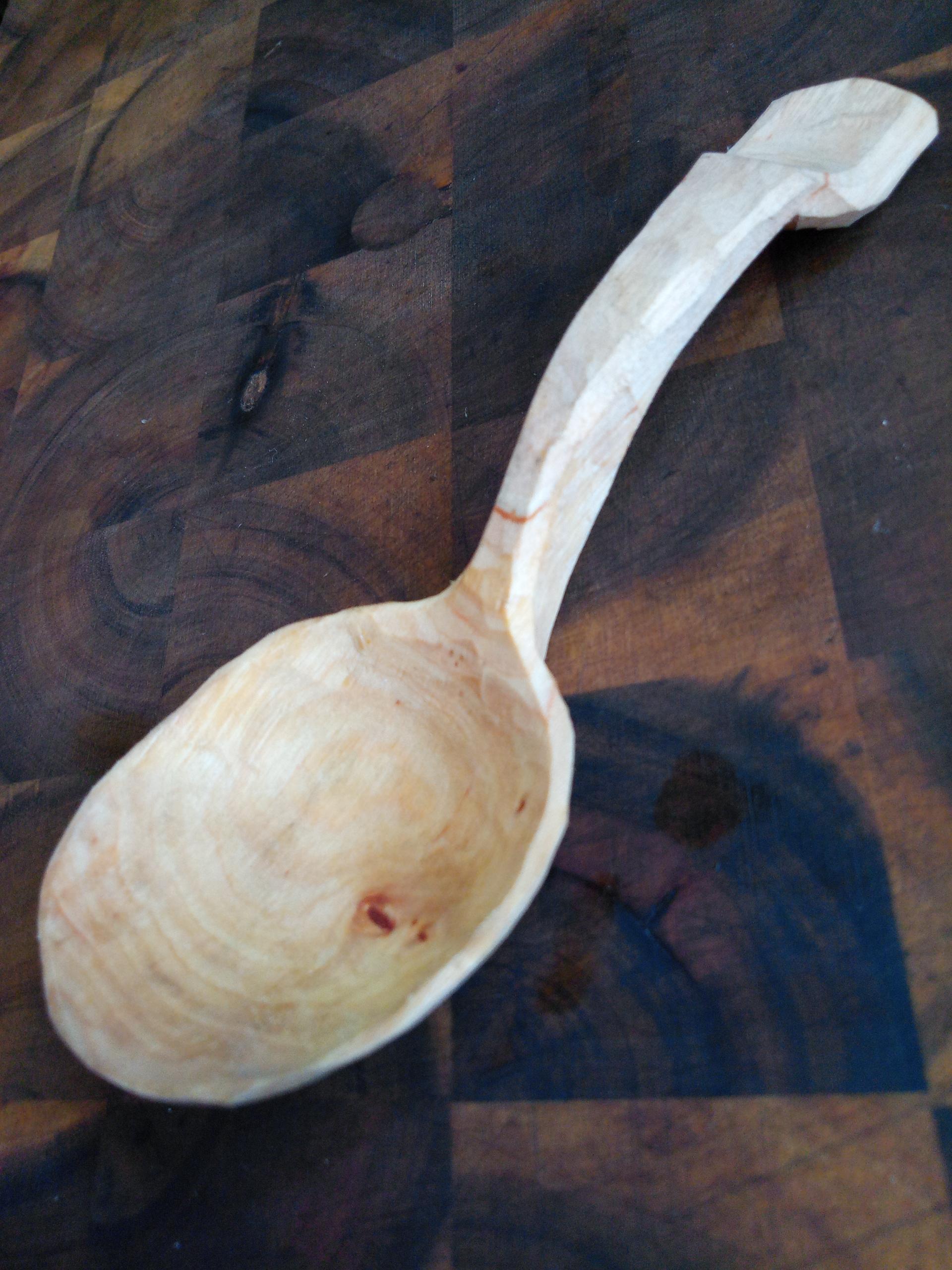 Ein heller, geschnitzter Holzlöffel liegt bilddiagonal auf dunkelbraunem Holz.
