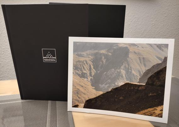 A black book in a black slipcase. On the front is a picture of a rugged, barren mountain landscape, in which a cyclist can be seen, very small, cycling up a road. 